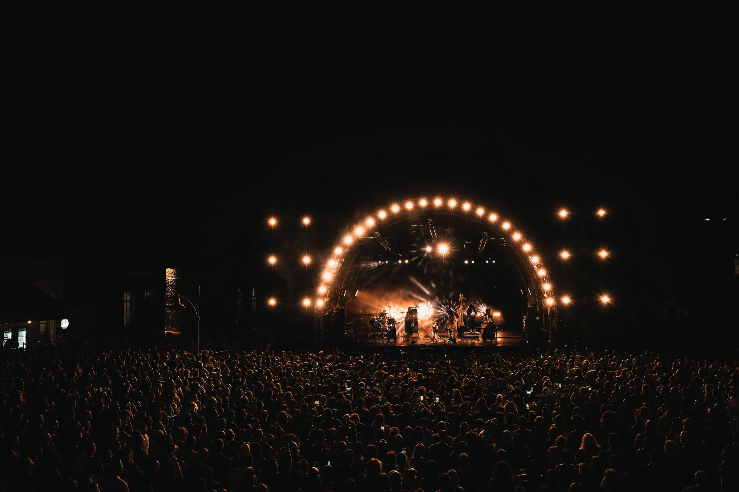 A night stage under an arch of warm lights, seen over a vast crowd
