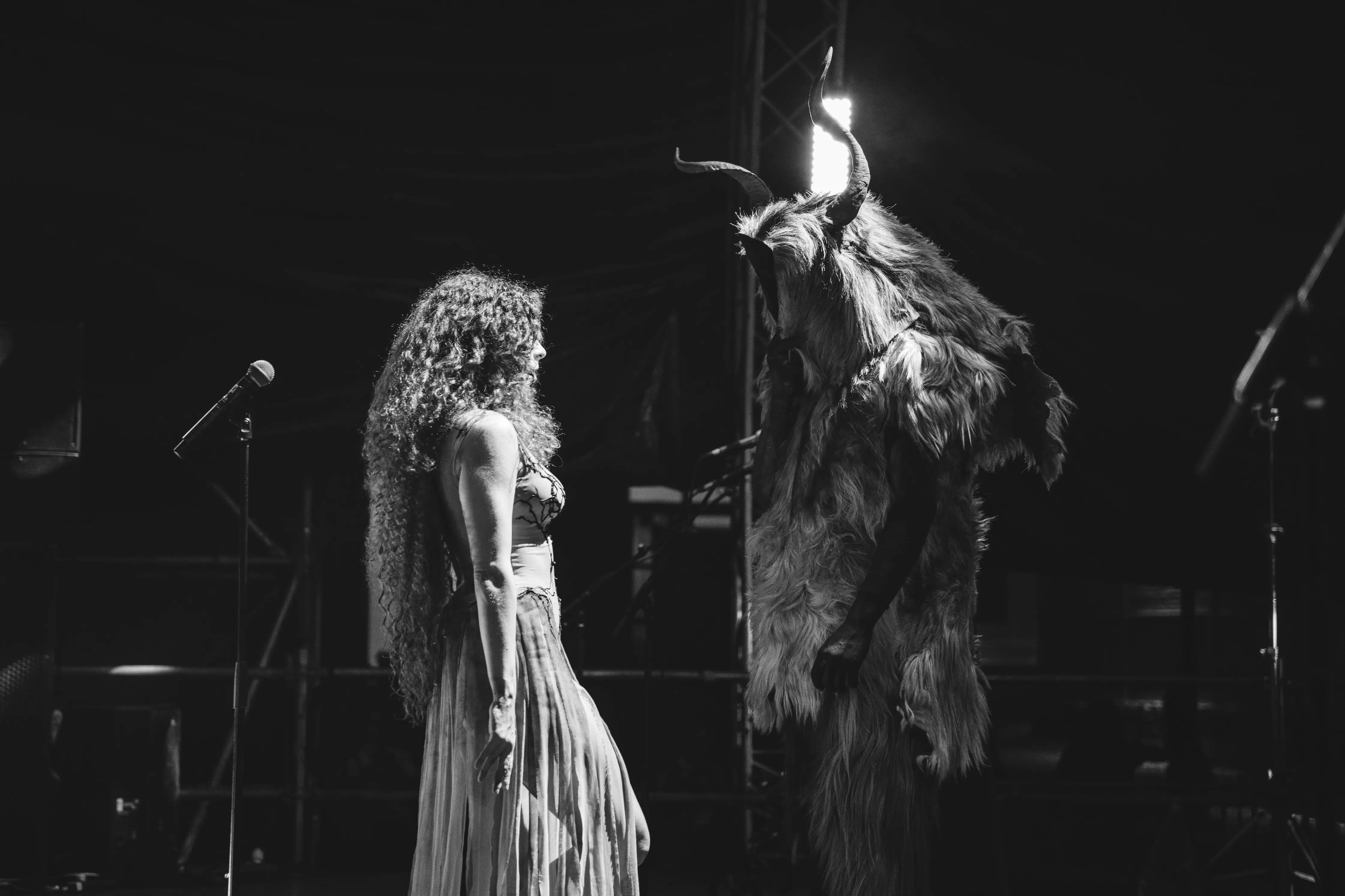 Evelyn Assouad face to face with a horned, fur-clad figure on stage, in black and white